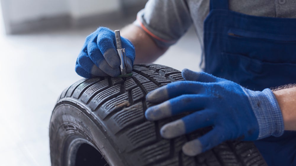 Technician checking tire tread depth with a tread gauge tool.